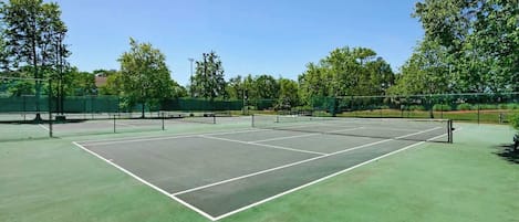 A tennis court with a net, surrounded by trees and a fence.