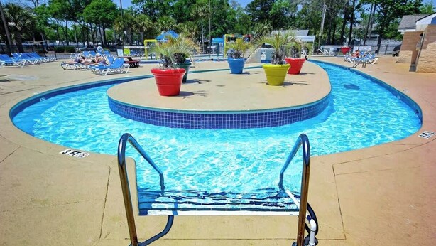 A swimming pool with a tiled edge, a pool ladder, and lounge chairs around the perimeter. - Myrtle Beach Resort A-332 (Myrtle Beach)