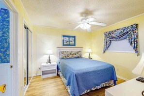 A bedroom with a bed, two bedside lamps, a ceiling fan, a window with curtains, and a door with a blue floral pattern. - Myrtle Beach Resort A-332 (Myrtle Beach)