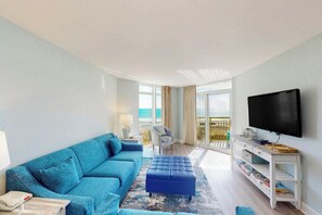 Ein modernes Wohnzimmer mit einem blauen Sofa, passendem Hocker, einem Flachbildfernseher und einem Balkon mit Aussicht.
