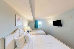 Ein Hotelzimmer mit zwei Betten, einem Flachbildfernseher, einem Gemälde an der Wand und einem Fenster mit Vorhängen.
