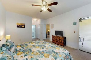 Ein Schlafzimmer mit einem Bett, einem Deckenventilator, einem Fernseher auf einer Kommode und einer Tür zu einem anderen Raum.