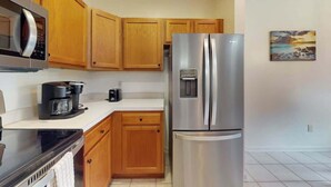 A kitchen with wooden cabinets, a stainless steel refrigerator, a microwave, and a coffee maker. - Legends Resort at Myrtle Beach Unit F (Myrtle Beach)