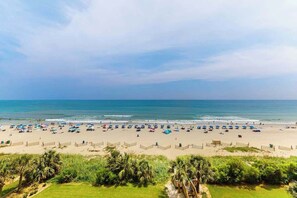 Une plage avec des parasols et des gens, des palmiers et un ciel dégagé.