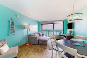 Ein Wohnzimmer mit einer Couch, einem Esstisch mit Stühlen, einer Chandelier und einem Balkon mit Blick.