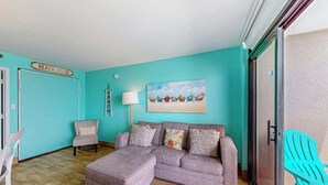 Een kamer met een blauwgroene muur, een grijze bank, een witte stoel, een blauwgroene stoel, en een schilderij van boten.