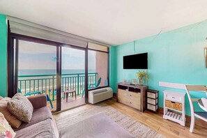 A room with a balcony, a sofa, a TV, and a small table. - Sandcastle South #616 (Myrtle Beach)