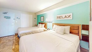 Een hotelkamer met twee bedden, een bordje met de tekst 'RELAX', een houten hoofdbord, een nachtkastje en een deur met een bordje.