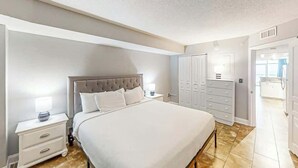 A bedroom with a large bed, a nightstand, a wardrobe, and a bathroom visible through an open door. - Bay Watch Resort 0919 (North Myrtle Beach)