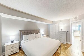A bedroom with a large bed, a nightstand, a wardrobe, and a bathroom visible through an open door. - Bay Watch Resort 0919 (North Myrtle Beach)