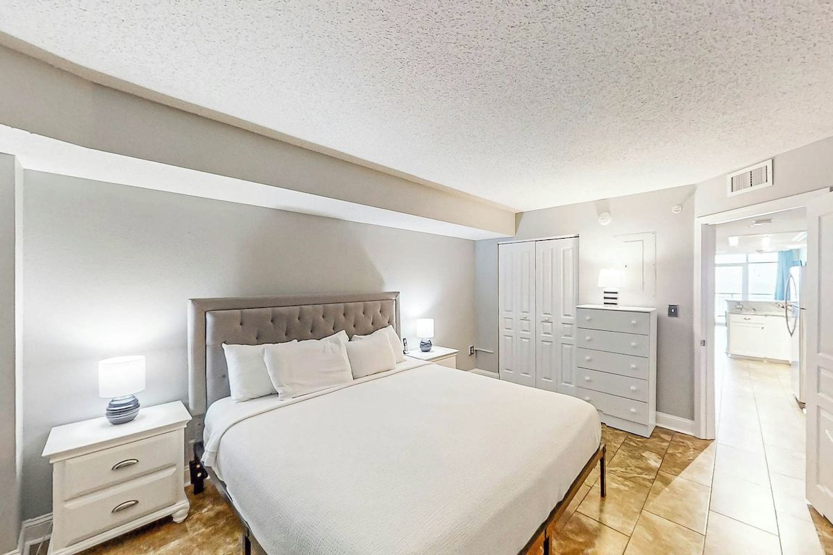 A bedroom with a large bed, a nightstand, a dresser, and a wardrobe.