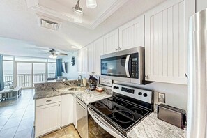 A kitchen with white cabinetry, a built-in microwave, a stove, and a toaster. - Bay Watch Resort 0919 (North Myrtle Beach)