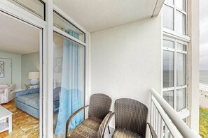 A balcony with wicker chairs, a view of the sea, and a room with a sofa and a lamp. - Bay Watch Resort 0919 (North Myrtle Beach)