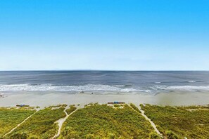 En strand med klar himmel, en sandstrand och en stig som leder till en byggnad.
