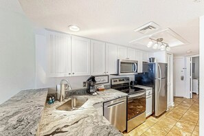 A modern kitchen with white cabinets, stainless steel appliances, and a marble countertop. - Bay Watch Resort 0919 (North Myrtle Beach)