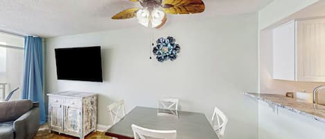 A dining area with a table, chairs, a ceiling fan, a television, and a cabinet.