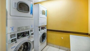 A laundry room with stacked washers and dryers, a wall-mounted control panel, and a whiteboard. - Bay Watch Resort 0919 (North Myrtle Beach)