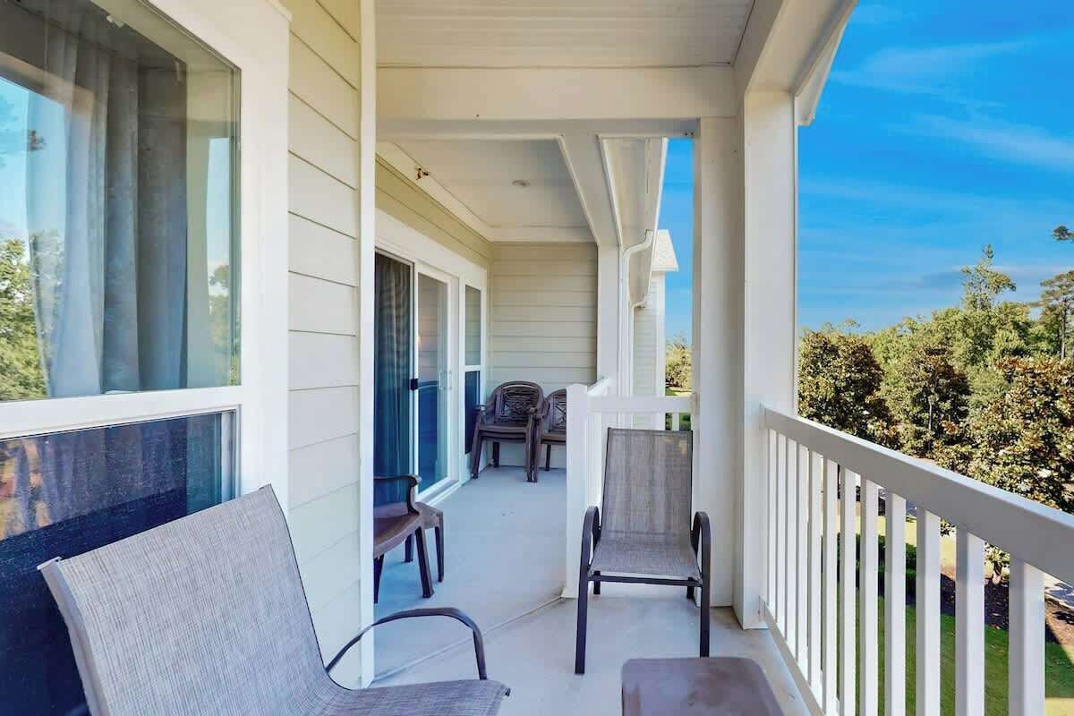 Une véranda avec deux chaises et une table, une vue dégagée sur l’extérieur et une balustrade blanche.