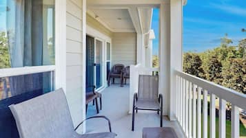 Une véranda avec deux chaises et une table, une vue dégagée sur l’extérieur et une balustrade blanche.