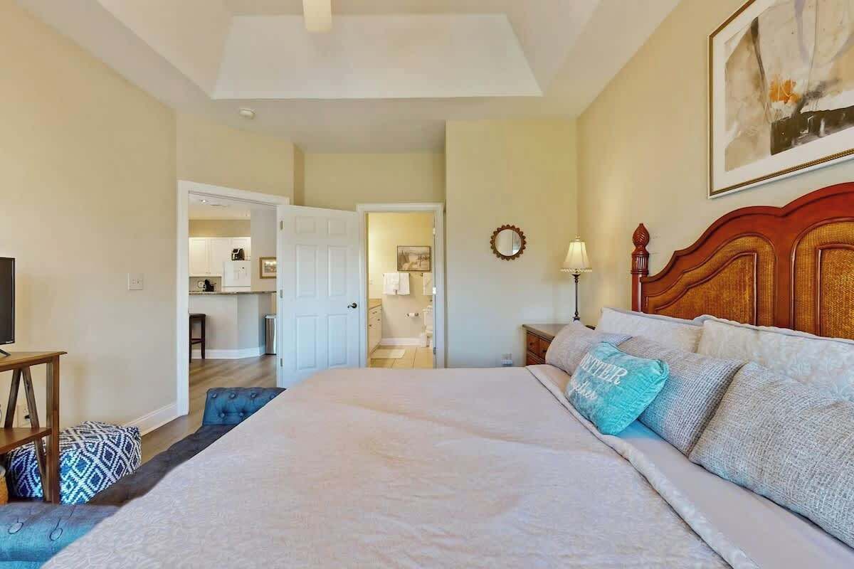 A hotel room with a large bed, a television, a desk, and a view of the kitchen and bathroom through an open door.