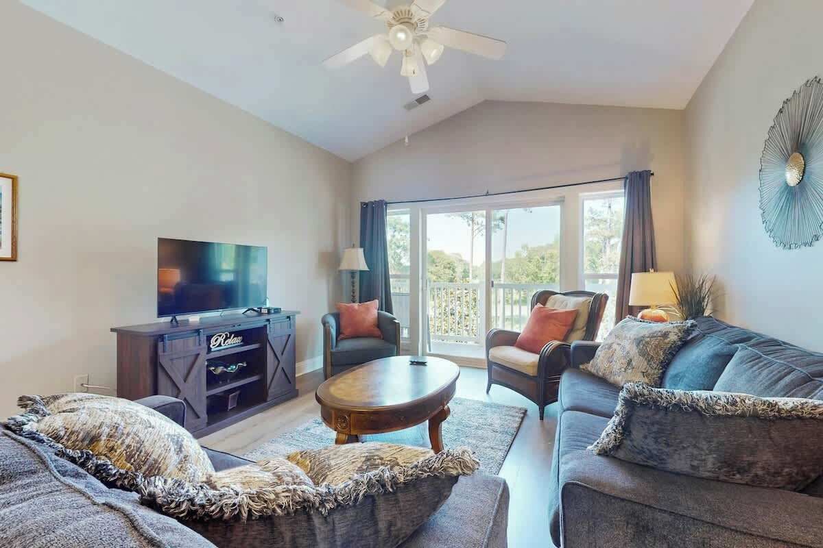 A living room with a flat-screen TV, a sofa, a coffee table, and a ceiling fan.