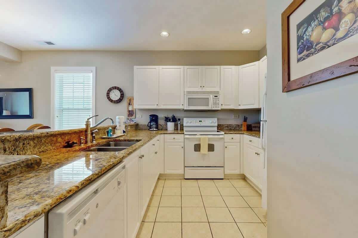 A kitchen with white cabinets, a granite countertop, a microwave, and a stove.