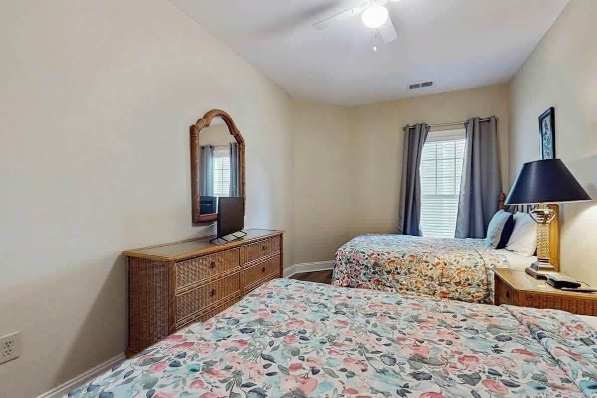 A bedroom with two beds, a dresser, a mirror, a ceiling fan, and a lamp.
