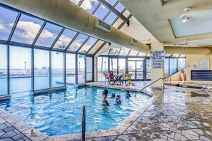 An indoor swimming pool with a view of the city skyline, a lifeguard sign, and a tiled floor. - Ocean Creek Unit PP3 (Myrtle Beach)