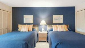 Een kamer met twee bedden, een nachtkastje met een lamp en twee ingekaderde foto's aan de muur.