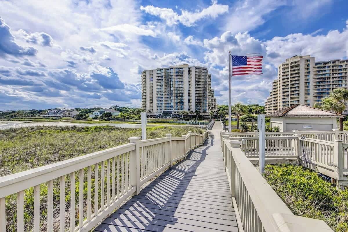 A wooden boardwalk leading to high-rise buildings with an American flag.