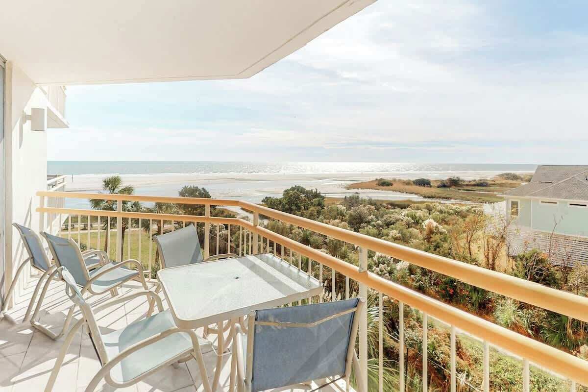 Un balcon avec une table et des chaises, donnant sur une plage et un paysage côtier.