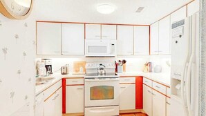 A compact kitchen with white cabinets, a microwave, a stove, and a refrigerator.