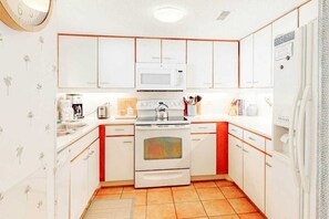 A compact kitchen with white cabinets, a microwave, a stove, and a refrigerator. - Ocean Creek Unit PP3 (Myrtle Beach)