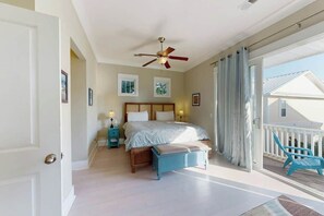 Quarto com cama, mesas de cabeceira, ventilador de teto e vista para o exterior.