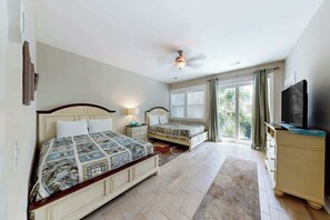 A bedroom with two beds, a ceiling fan, a television on a dresser, and a window with curtains. - Seas the Day Retreat (Myrtle Beach)