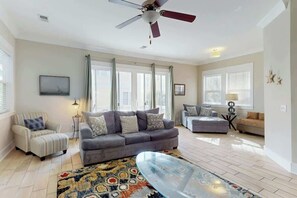 A spacious living room with a grey sofa, a patterned rug, and a ceiling fan. - Seas the Day Retreat (Myrtle Beach)