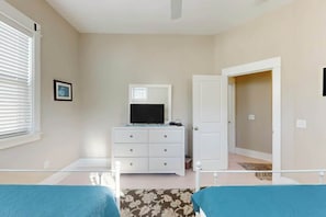 Une chambre à coucher avec un lit, une commode, un miroir, une porte et une fenêtre avec des stores.