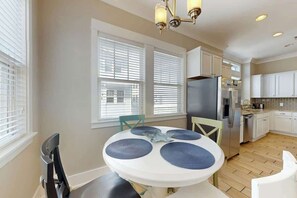 A kitchen with white cabinets, a stainless steel refrigerator, and a round table with blue placemats. - Seas the Day Retreat (Myrtle Beach)