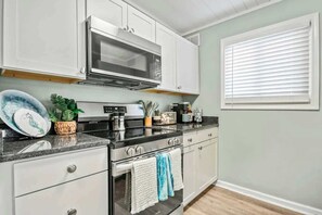 A kitchen with white cabinets, a stainless steel stove, a microwave, and a window with blinds. - Waipani Unit D-12 Condo (North Myrtle Beach)