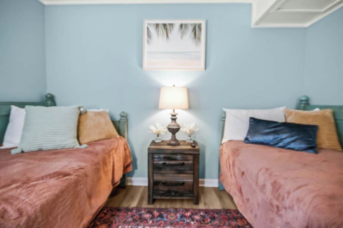 A bedroom with two beds, a nightstand with a lamp, and a framed picture on the wall.