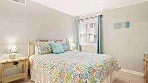 A bedroom with a bed, nightstands, a window with blinds, and a wall decoration. - Waipani Unit D-10 Condo (North Myrtle Beach)