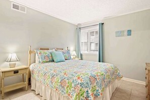 A bedroom with a bed, nightstands, a window with blinds, and a wall decoration. - Waipani Unit D-10 Condo (North Myrtle Beach)