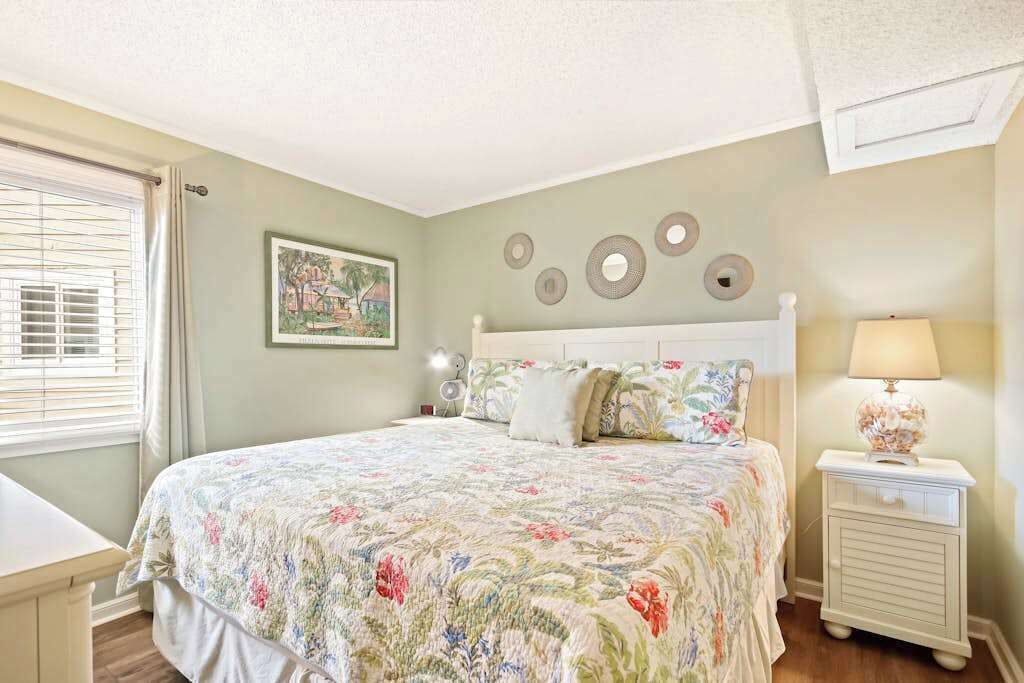 A bedroom with a bed, bedside table, lamp, and wall decor.
