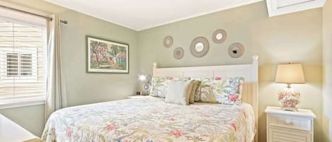 A bedroom with a bed, bedside table, lamp, and wall decor.