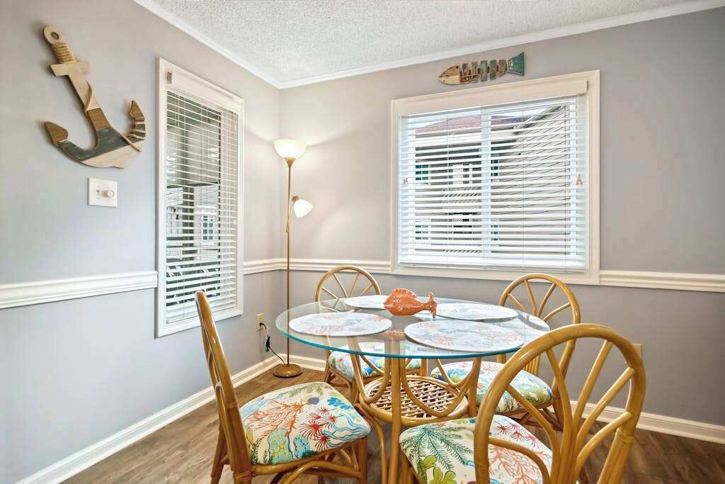 Un comedor con una mesa redonda de cristal, sillas de mimbre y un ancla decorativa en la pared.