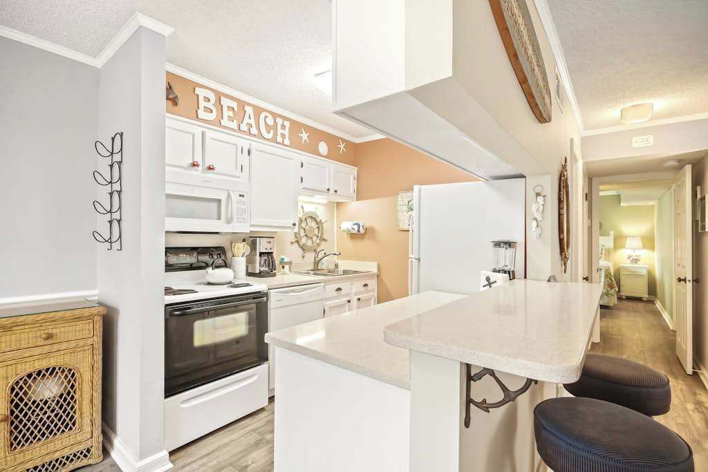 A kitchen with white cabinets, a central island, and a 'BEACH' sign.