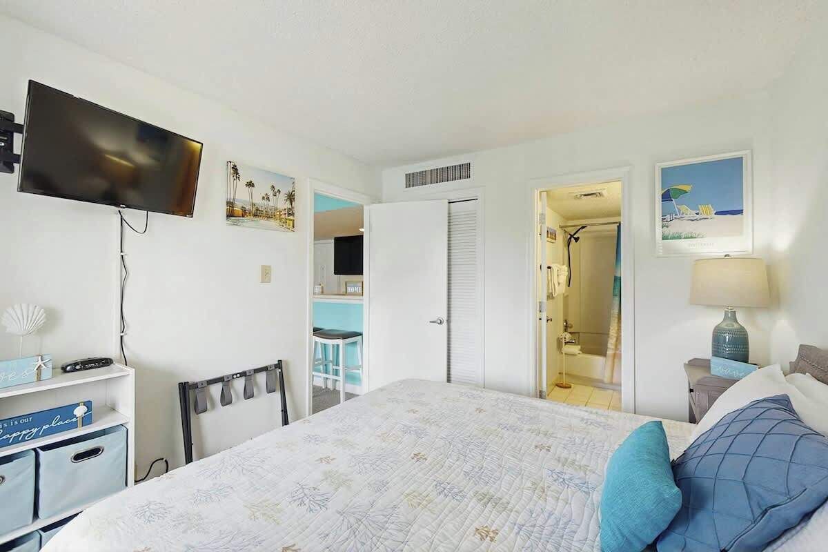 A hotel room with a bed, a television, a desk with a lamp, and a bathroom visible through an open door.