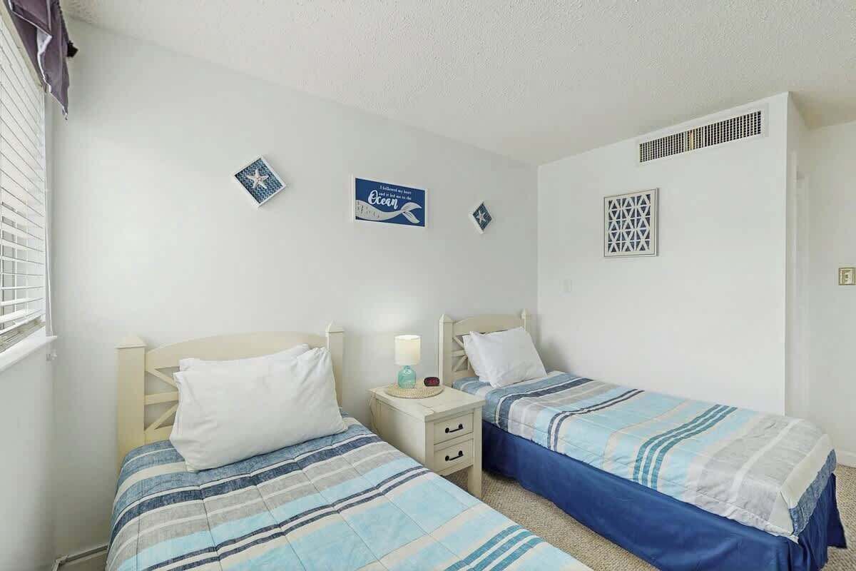 A bedroom with two beds, a nightstand, and a wall-mounted shelf.