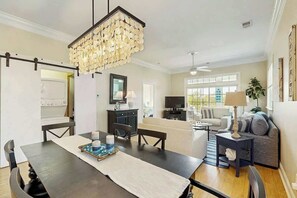 A modern living room with a dining area, a chandelier, and a television. - Seaside Sanctuary at Litchfield by the Sea (Pawleys Island)