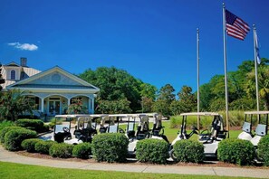 A golf course with a clubhouse, golf carts, and American flags. - Seaside Sanctuary at Litchfield by the Sea (Pawleys Island)